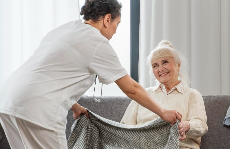 Caregiver placing blanket over elderly womans lap